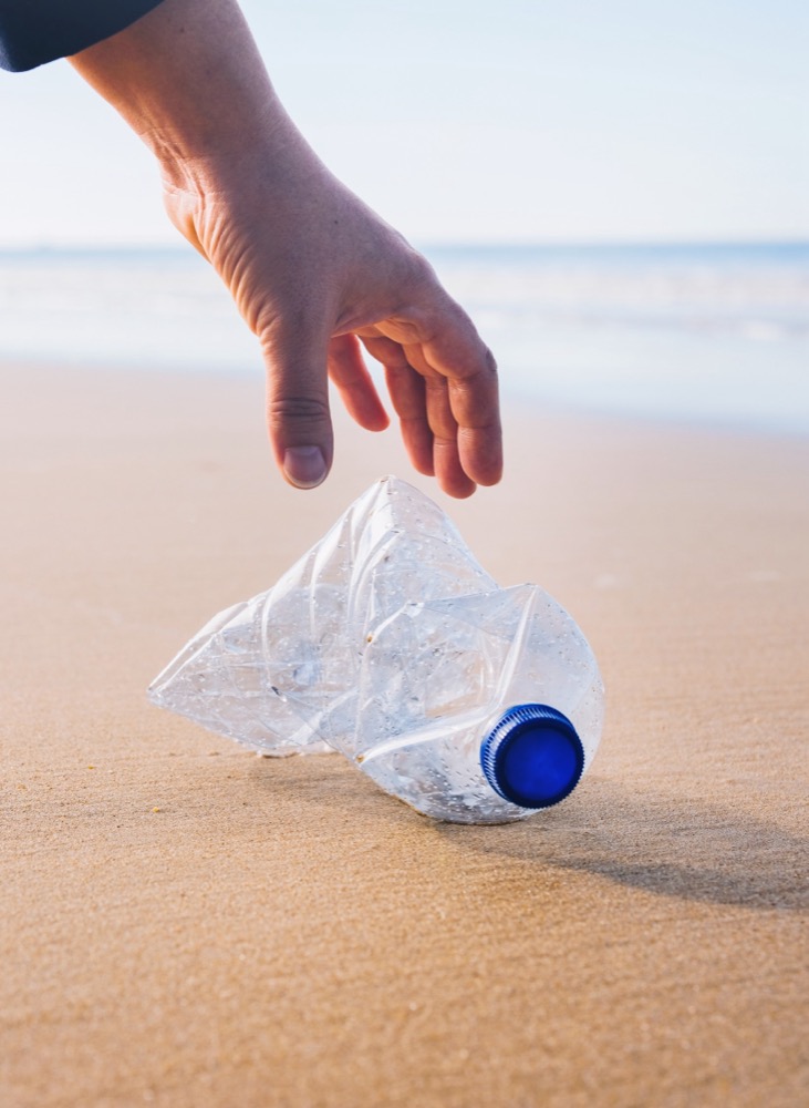 Mano recolectando una botella de plástico en la playa